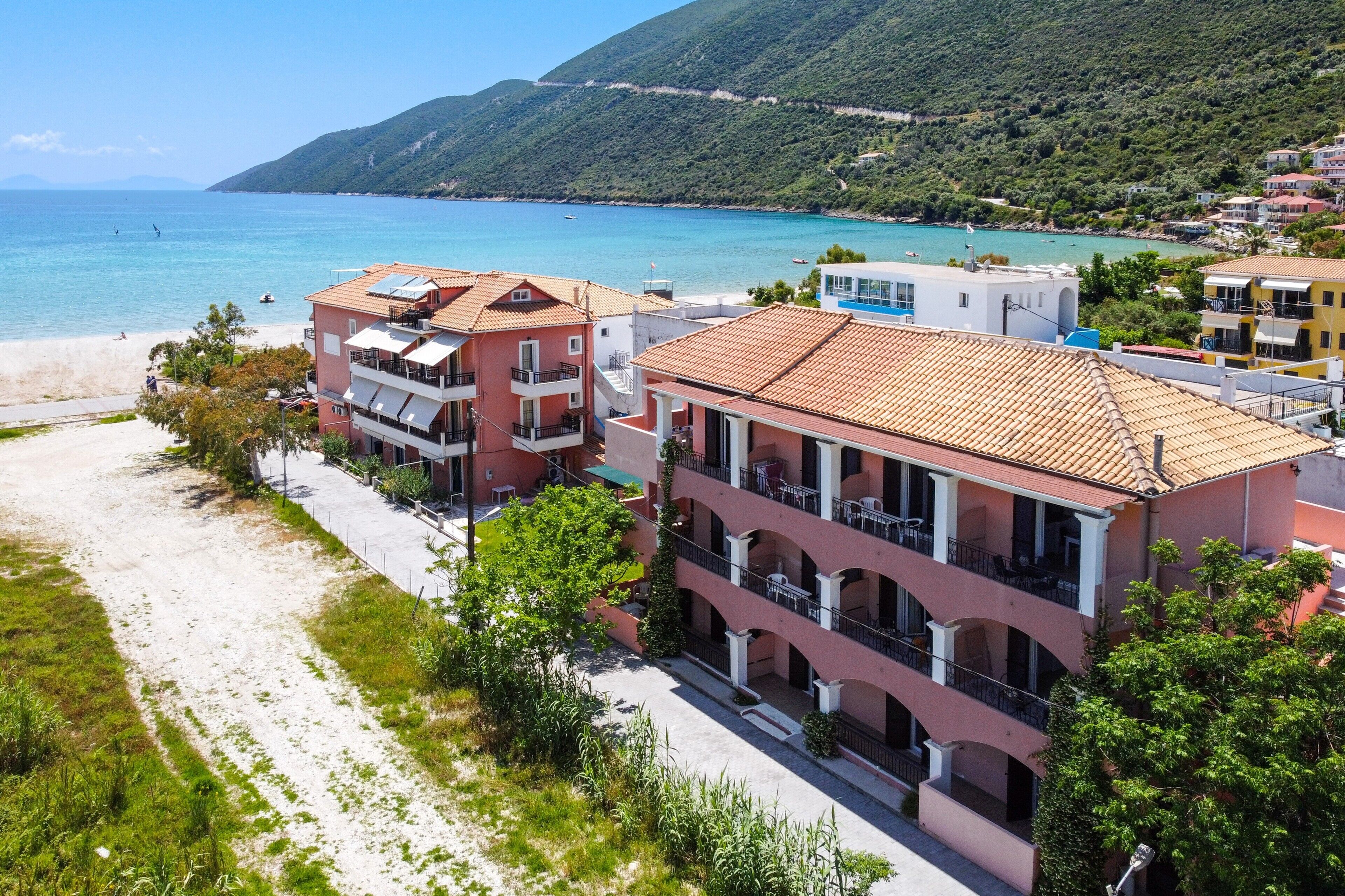 Un hotel frente al mar con varios balcones, una playa y montañas al fondo.