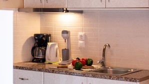 Une cuisine équipée d’une machine à café, d’un extracteur de jus, d’un évier et de quelques légumes posés sur le plan de travail.