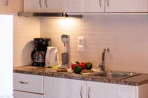 A kitchen with a coffee maker, a juicer, a sink, and some vegetables on the counter.