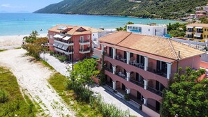 A coastal hotel with multiple balconies, a beach, and a mountainous backdrop.