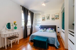 A bedroom with a bed, a vanity with a mirror, a bench, and a window with curtains.