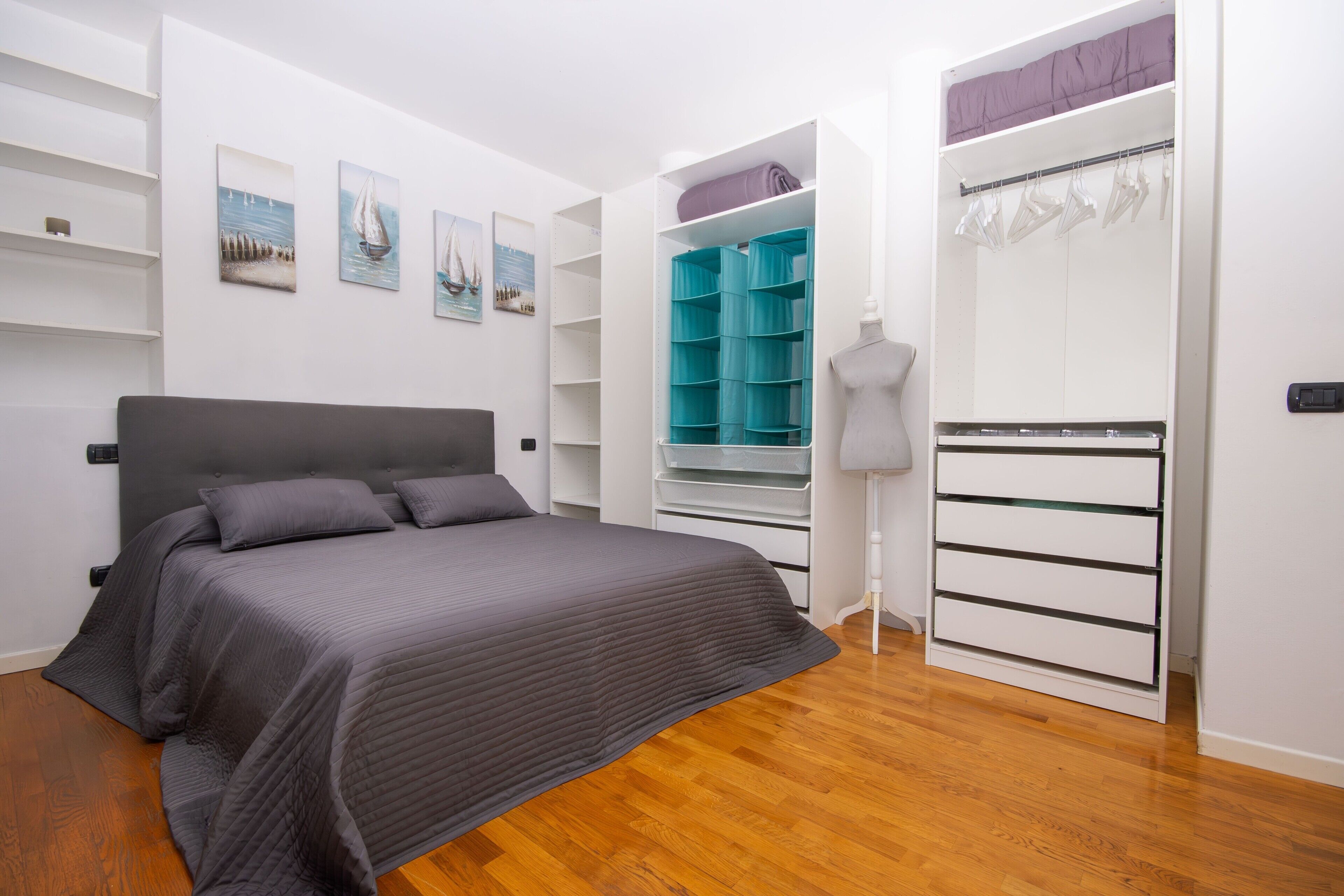 Une chambre à coucher comprenant un lit, une armoire et une étagère où sont exposées des œuvres d’art.