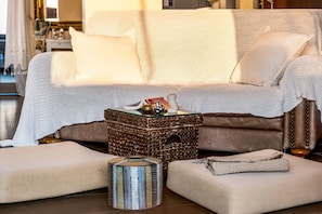Un salon chaleureux avec un canapé beige, une table basse en osier et une petite table d’appoint.