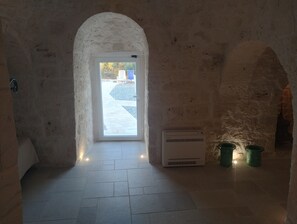 An arched doorway leading to an outdoor area with a tiled floor, a wall-mounted air conditioning unit, and two green buckets. - Villa "Trullo Libellula" with Private Garden, Private Pool, and Wi-Fi (Ceglie Messapica)