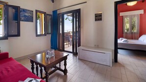 A room with a wooden table, a red sofa, a bed with white bedding, and a sliding glass door leading to an outdoor area. - Apartment 'Villa Rojo Tajo Villas' with Sea View, Wi-Fi and Air Conditioning (Lefkada)