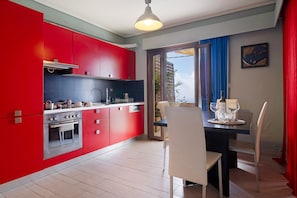 Une cuisine moderne avec des meubles rouges, un coin repas comprenant une table et des chaises, et une vue à travers une porte vitrée.