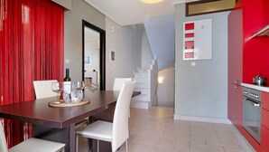 A modern kitchen with a red cabinet, a dining area with a wooden table and white chairs, and a staircase leading to an upper level. - Apartment 'Villa Rojo Tajo Villas' with Sea View, Wi-Fi and Air Conditioning (Lefkada)