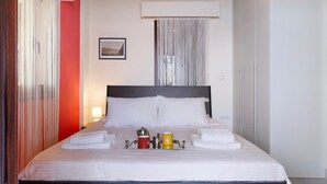 A hotel room with a bed, a bedside table, a window with curtains, a wall-mounted air conditioning unit, and a framed picture on the wall. - Apartment 'Villa Rojo Tajo Villas' with Sea View, Wi-Fi and Air Conditioning (Lefkada)