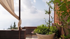 A balcony with a potted plant, a wooden bench, and a view of the sky.
