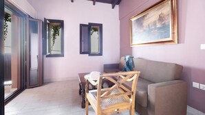 A room with a wooden chair, a sofa, a table, and a painting on the wall.