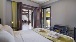 A hotel room with a bed, a bedside table, a lamp, a mirror, and an open door leading to a dining area.