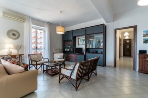 A living room with a sofa, chairs, a coffee table, a TV, and a bookshelf.