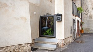 A narrow street with a building featuring a small set of steps leading to a door with a framed picture of a waterfall.