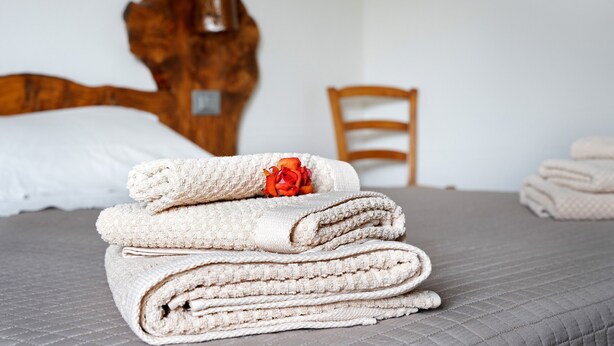 A neatly made bed with a folded towel stack and a single rose.