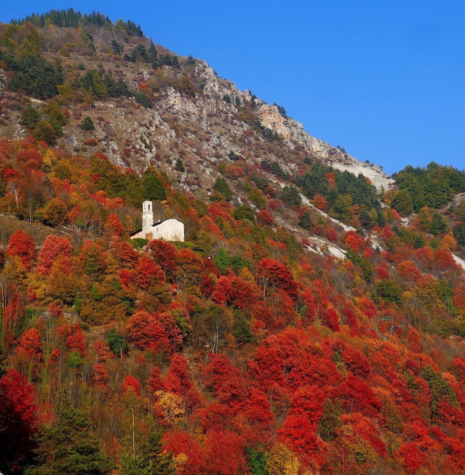 Eine Berglandschaft mit einem weißen Gebäude, wahrscheinlich ein Hotel, umgeben von Bäumen in Herbstfarben.