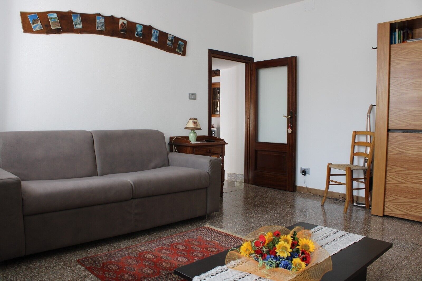 Un saló amb un sofà, un armari de fusta, una porta i una taula petita amb un arranjament floral.