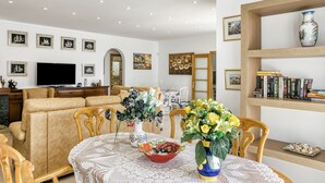 Una sala de estar con un sofá, un televisor, una mesa de comedor con sillas y una estantería.