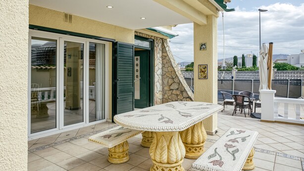 Un patio al aire libre con una mesa, bancos, una puerta corrediza de vidrio y un muro de piedra.