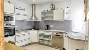 Una cocina moderna con armarios blancos, extractor de acero inoxidable, lavavajillas y horno empotrado.