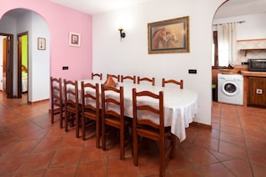 A dining area with a round table and wooden chairs, a kitchen with a washing machine, and a painting on the wall.