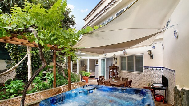 Un bain à remous situé dans un espace extérieur abrité, agrémenté d’une pergola, d’une table à manger et de chaises.