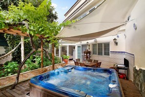 Un bain à remous situé dans un espace extérieur abrité, agrémenté d’une pergola, d’une table à manger et de chaises.