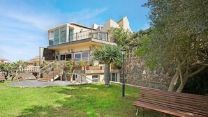 Une maison moderne à deux étages, dotée d’un balcon, d’un mur en pierre et d’une cour gazonnée.