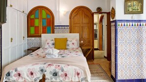 Une chambre à coucher avec un lit, une armoire en bois, une porte avec un miroir et un mur recouvert de carreaux.