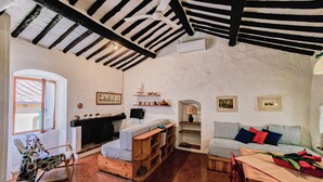 Una habitación rústica con vigas a la vista, una chimenea, un sofá, una mesa de madera y una ventana con vistas.