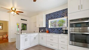 A modern kitchen with white cabinets, a blue backsplash, and stainless steel appliances. - The Charlotte House - Pool, Hot tub, Night of Lights! (Downtown St. Augustine)