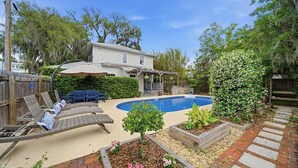 A backyard with a swimming pool, lounge chairs, a wooden deck, and a garden with flowering plants. - The Charlotte House - Pool, Hot tub, Night of Lights! (Downtown St. Augustine)