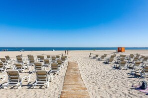 A beach with rows of sun loungers and a wooden walkway leading to the water.