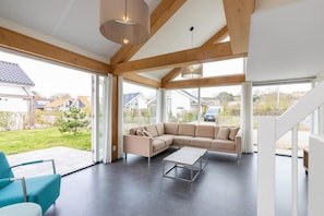 A modern living room with a sectional sofa, a coffee table, and a view of a residential area through large windows.