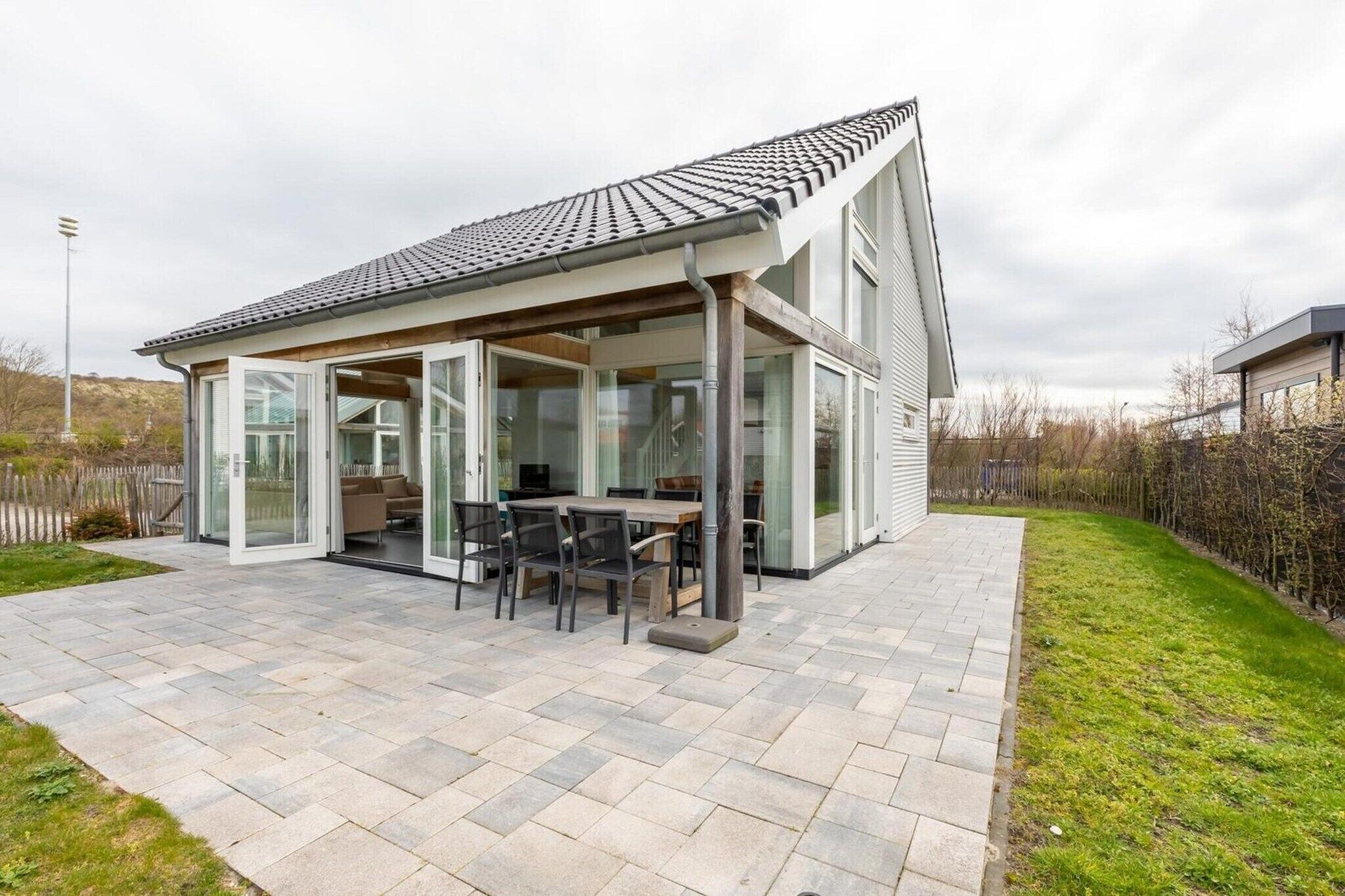 Una casa moderna con un patio, un comedor con sillas y una mesa, y un amplio ventanal que da al interior.