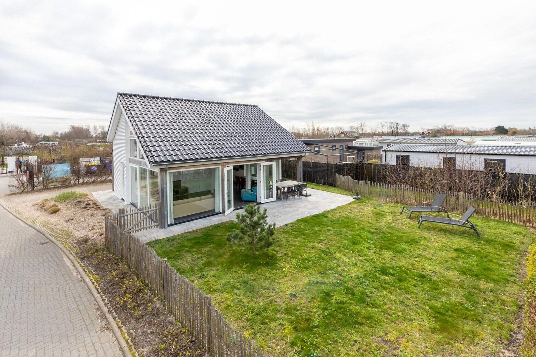 Una casa moderna con techo inclinado, puerta de cristal y un pequeño jardín con un banco.