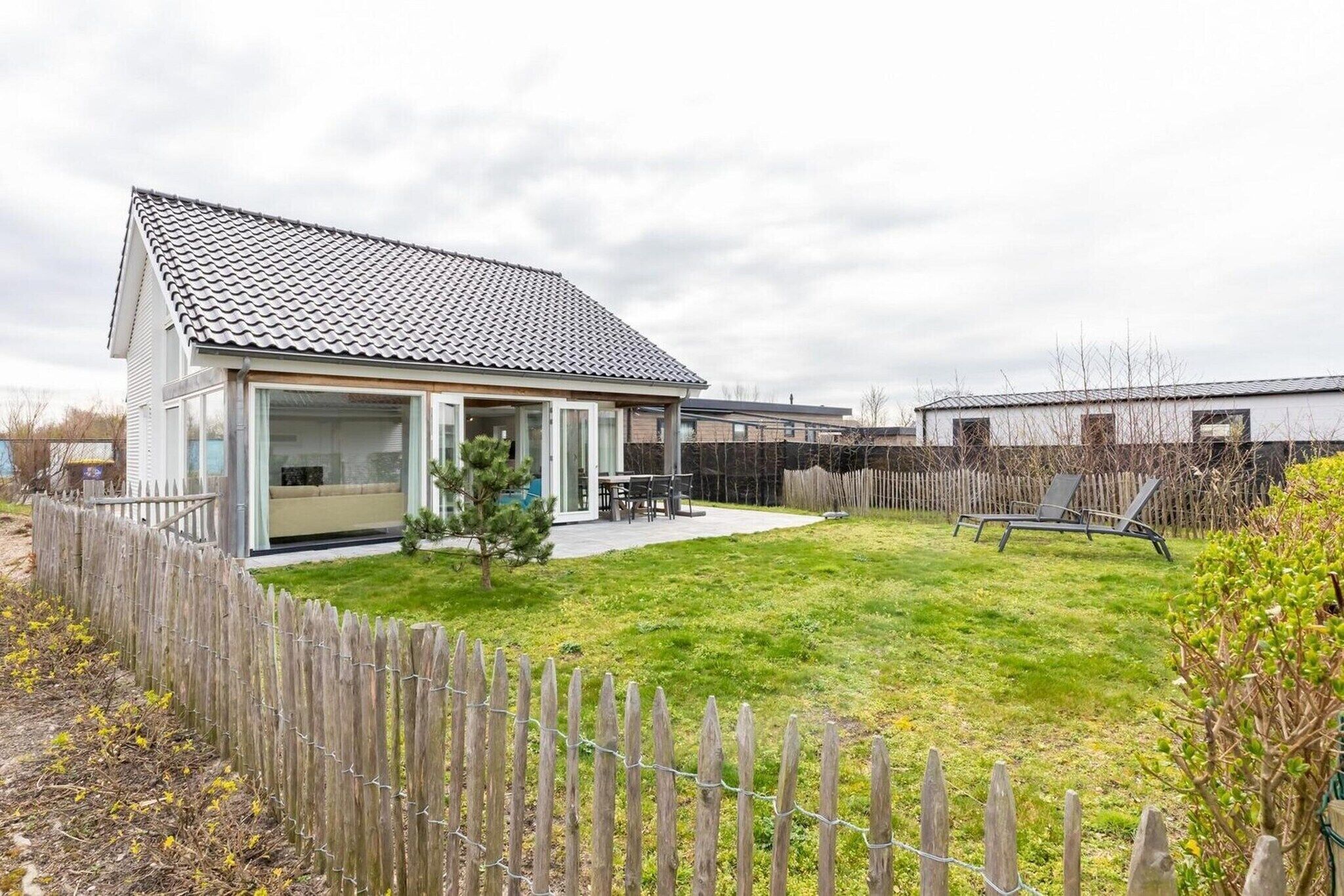 Une maison de plain-pied avec un toit en tuiles, une cour arrière clôturée et un petit espace patio.