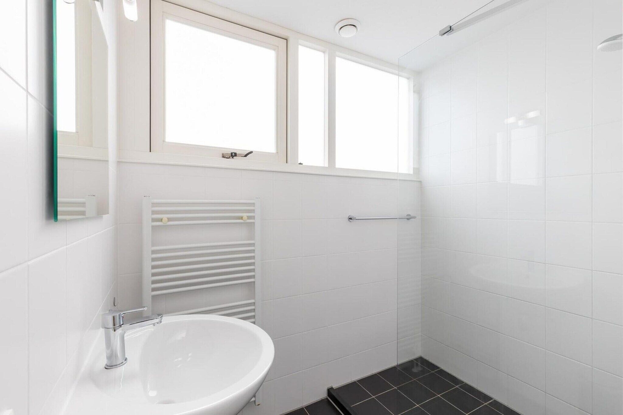 A bathroom with a white sink, a mirror, a towel rack, and a shower area.