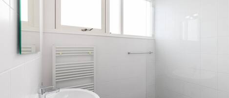 A bathroom with a white sink, a mirror, a towel rack, and a shower area.