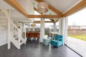 A modern interior with a staircase, dining area, and seating by a large window.