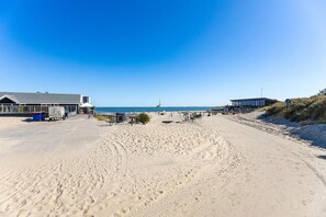 A beachside property with a paved walkway, a building with a metal roof, and a sandy beach area. - Holiday Home in Renesse near the Beach (Renesse)