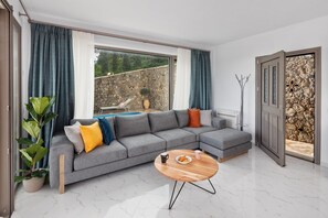 A modern living room with a grey sectional sofa, a round wooden coffee table, and a large window with curtains.