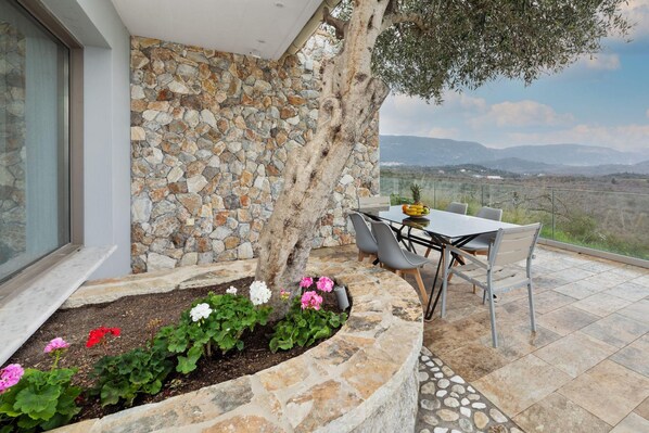 An outdoor dining area with a stone wall, a tree, and a view of the landscape.