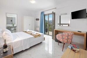A hotel room with a bed, a desk, a chair, a TV, and a balcony with a view.
