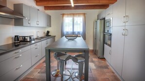 A modern kitchen with grey cabinets, a stainless steel range hood, a built-in oven, and a window with sheer curtains.