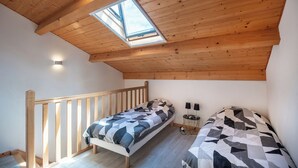 A small, cozy bedroom with a sloped ceiling and a skylight, featuring two beds with geometric-patterned bedding.