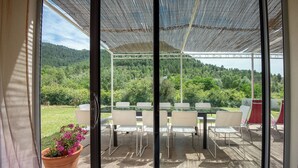 A covered patio with a table and chairs, a potted plant, and a view of a forested hillside.