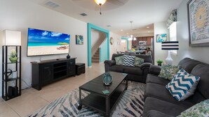 A modern living room with a flat-screen TV, dark furniture, a ceiling fan, and a staircase leading to a kitchen. - Coastal Decor-Hen's Nest- Privacy-Pool & Spa- Gated Community (Davenport)