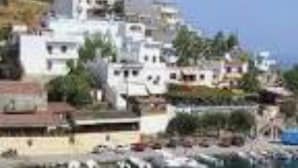 A coastal town with buildings along the waterfront, a marina with boats, and a clear sky.