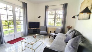 Un salon moderne avec un canapé, une table basse, un téléviseur et une vue sur la verdure grâce à de grandes fenêtres.