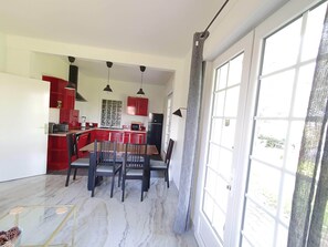 A modern kitchen with red cabinets, a dining area with a marble floor, and large windows providing natural light.